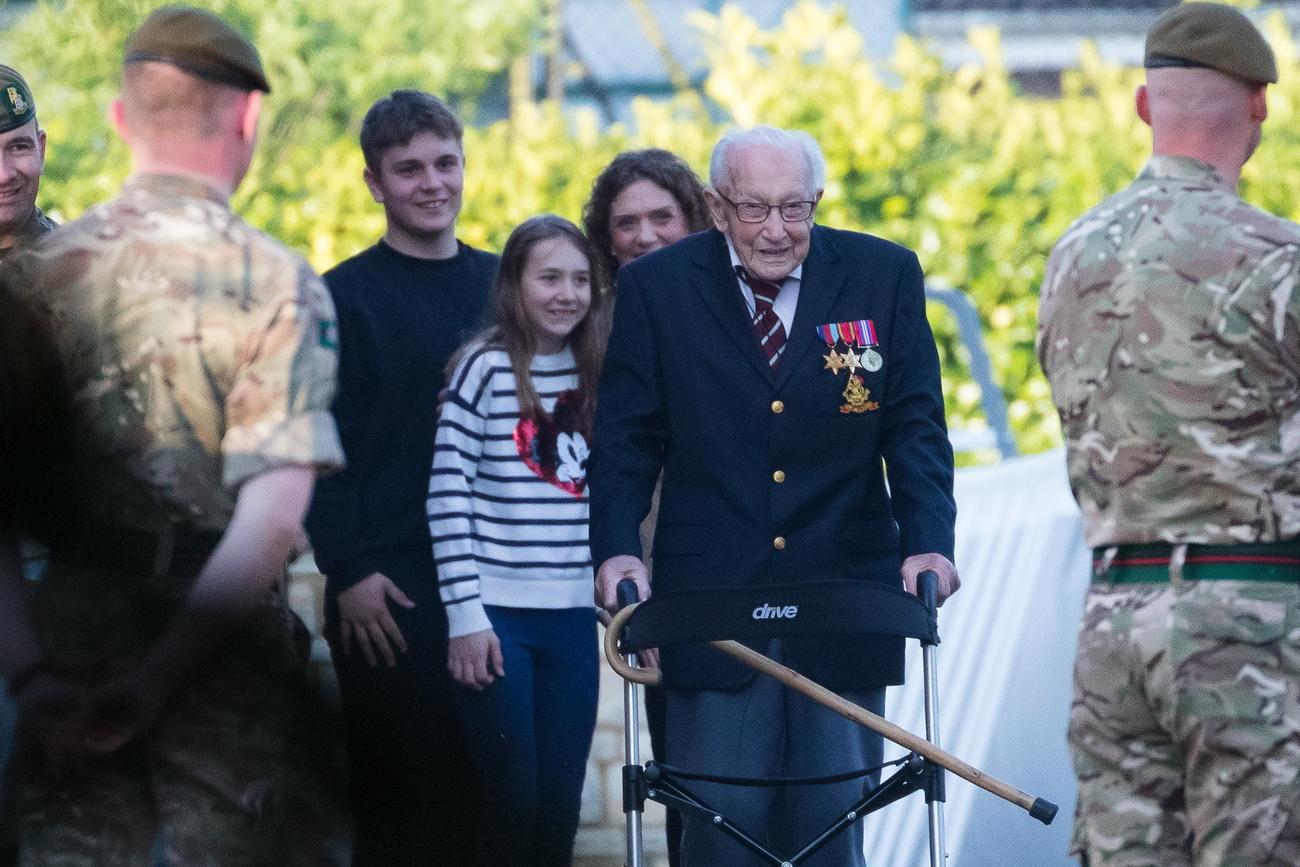 Le capitaine Tom Moore, 99 ans, termine son 100e trajet sous les yeux de sa famille. Il est salué par des militaires venus le féliciter. [Keystone/epa - Vickie Flores]