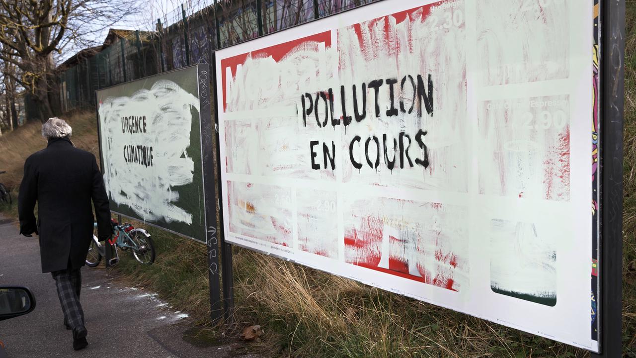 Affiches publicitaires recouvertes de peinture avec le message "Pollution en cours" à Genève le 12 mars 2019. [Keystone - Salvatore Di Nolfi]