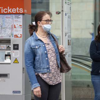 Des personnes portant un masque attendent à un arrêt de bus à Genève. [Keystone - Martial Trezzini]
