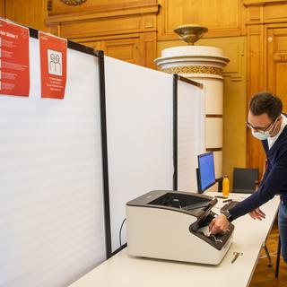 Un scrutateur scanne les bulletins de vote lors des élections communales dans le canton de Neuchâtel. [Keystone - Jean-Christophe Bott]