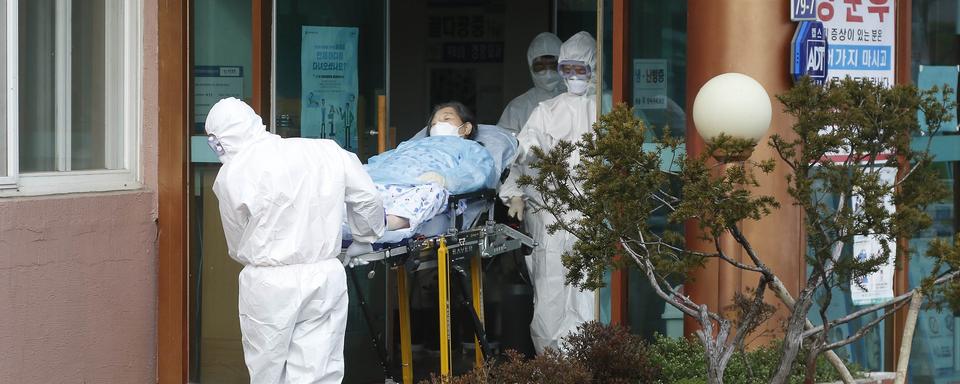 Des pompiers transportent une patiente atteinte du coronavirus à l'Hôpital de Cheongdo (en Corée du Sud). [AFP - Seung-il Ryu / NurPhoto]