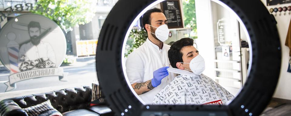 Un coiffeur et son client, portant des masques, le jour de la réouverture des salons de coiffure, le 27 avril 2020 à Lausanne. [Keystone - Jean-Christophe Bott]