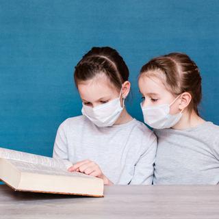 Deux enfants qui portentent un masque cherchent un mot dans le dictionnaire. [Depositphotos - Aleruana]