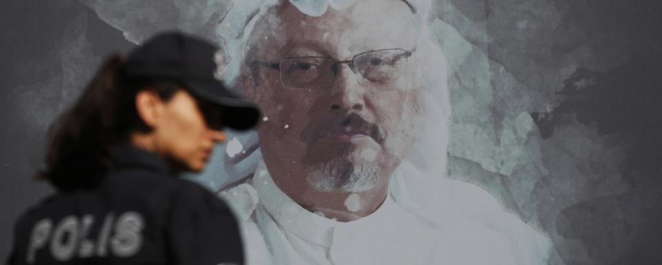 Une policière turque passe devant un portrait du journaliste Jamal Khashoggi, assassiné dans le consulat d'Arabie Saoudite à Istanbul. Octobre 2019. [Keystone/ap photo - Lefteris Pitarakis]