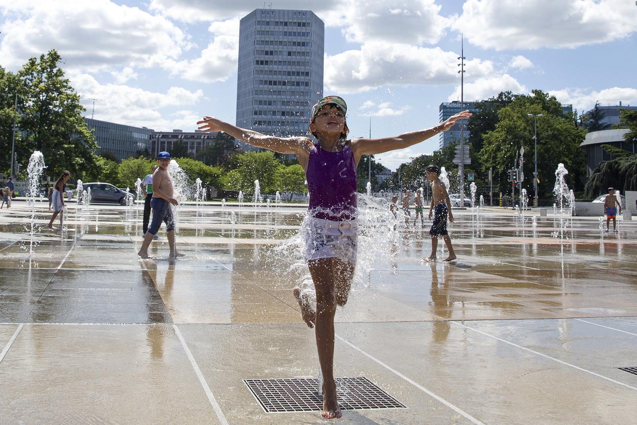 Des enfants jouent au milieu des jets d'eau sur la place des Nations à Genève, le 23 août 2020. [Keystone - Salvatore Di Nolfi]