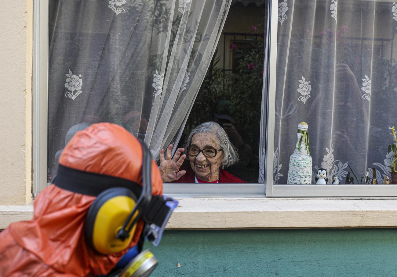 Une femme salue une personne en train de désinfecter les rues de son quartier. Santiago, Chili, le 15 avril 2020. [Keystone/ap photo - Esteban Felix]