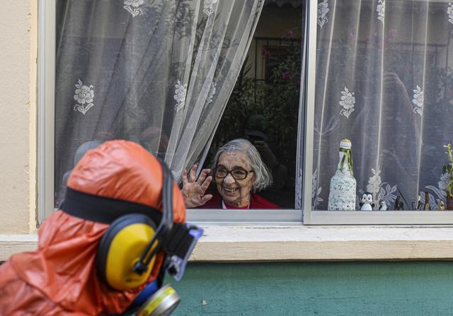 Une femme salue une personne en train de désinfecter les rues de son quartier. Santiago, Chili, le 15 avril 2020. [Keystone/ap photo - Esteban Felix]