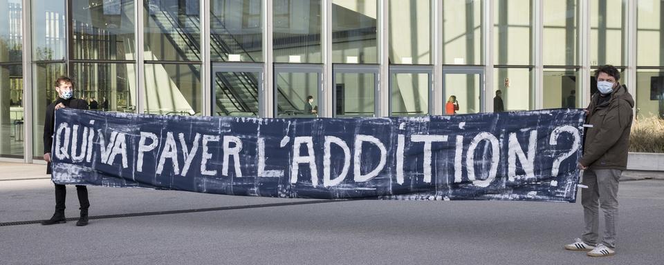 Des manifestant tiennent une banderole avec l'inscription "Qui va payer l'addition?", le 17 novembre 2020 sur le site de l'EPFL. [Keystone - Cyril Zingaro]