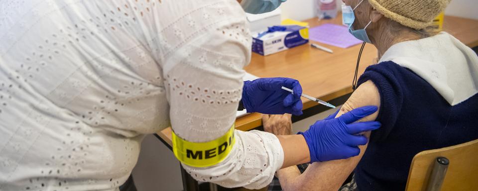 Une infirmière donne la première dose de vaccin à une patiente âgée au centre de vaccination de Cernier (NE), le 28 décembre 2020. [Keystone - Jean-Christophe Bott]