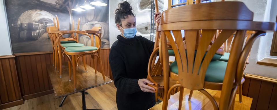 Une femme range les chaises d'un restaurant à Nyon, le 4 novembre 2020. [Keystone - Martial Trezzini]