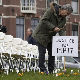 Rob Fredriksz, qui a perdu son fils Bryce et son amie Daisy, plante un panneau à côté des 298 chaises vides représentant chacune une des victimes du vol MH17 de Malaysia Air. Les chaises sont installées dans un parc en face de l'Ambassade russe à La Hague. Pays-Bas, le 8 mars 2020. [Keystone/ap photo - Peter Dejong]