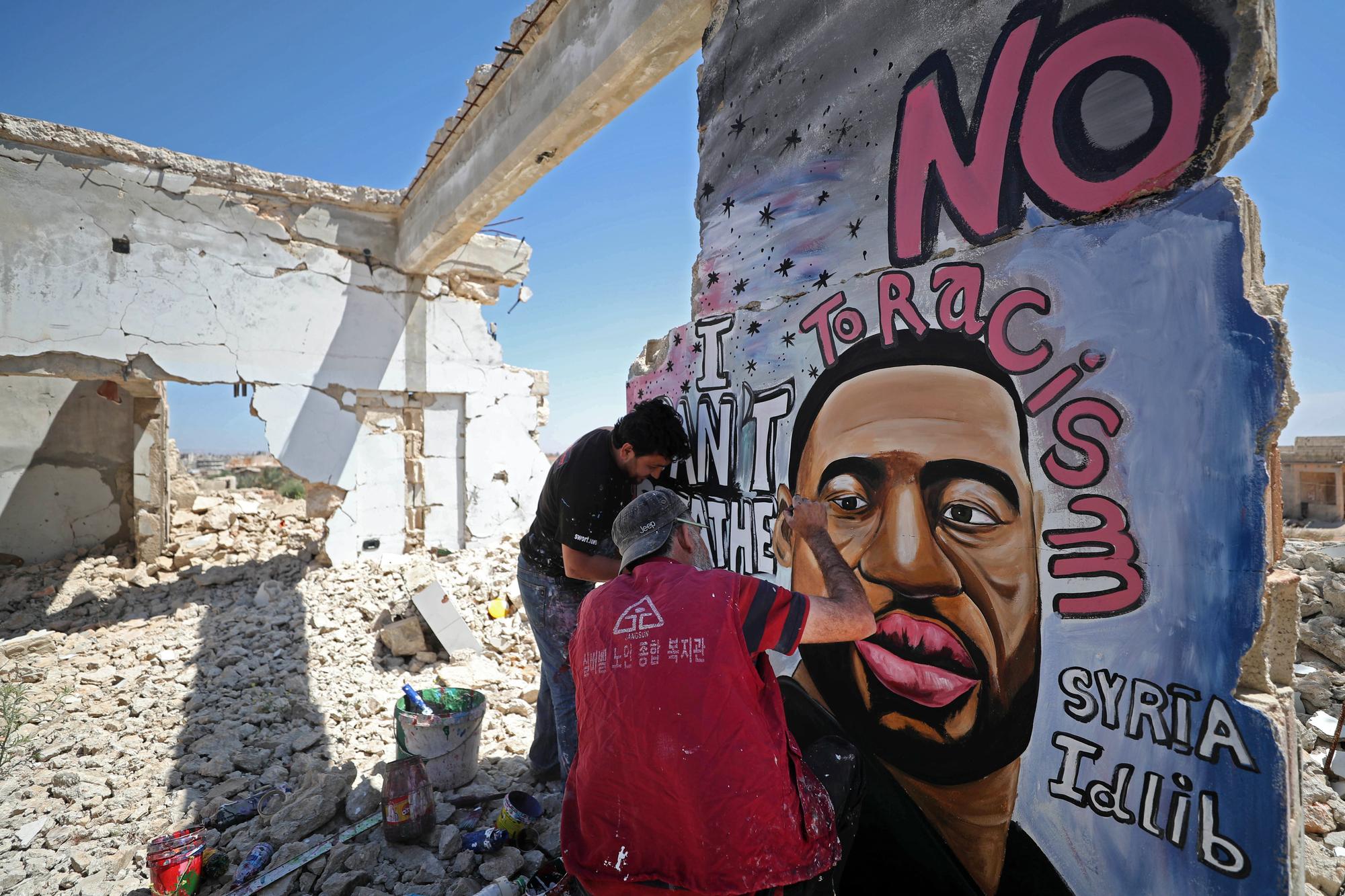 Les artistes syriens Aziz Asmar et Anis Hamdoun peignent le visage de George Floyd sur le mur d'un immeuble détruit à Binnish, dans la province d'Idleb. [AFP - OMAR HAJ KADOUR]