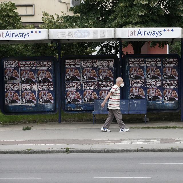Un homme passe devant des affiches électorales en Serbie. [AP Photo/Keystone - Darko Vojinovic]