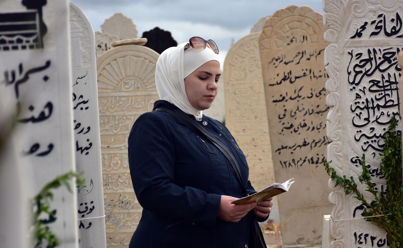 En Syrie, à l'occasion de l'Aïd, une musulmane lit le coran sur la tombe de ses proches dans le cimetière de Damas. [Keystone - YOUSSEF BADAWI]