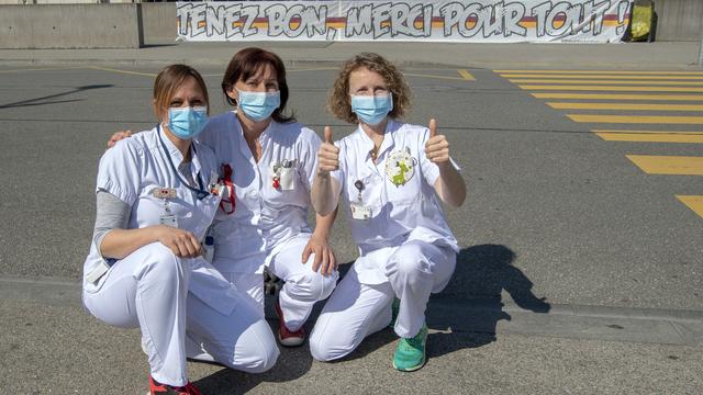 Des infirmières des Hôpitaux Universitaires de Genève (HUG) posent devant une banderole "Tenez Bon, Merci Pour Tout!": elles remercient la population de les soutenir tous les soirs à 21h00. Genève, le 19 mars 2020. [Keystone - Martial Trezzini]