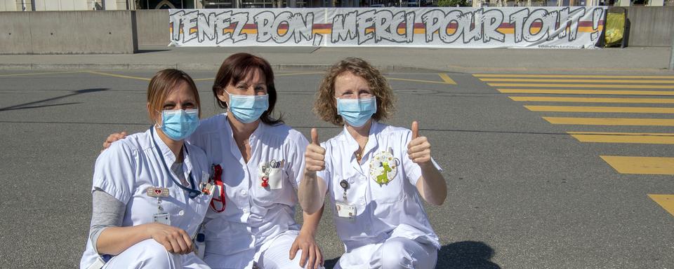 Des infirmières des Hôpitaux Universitaires de Genève (HUG) posent devant une banderole "Tenez Bon, Merci Pour Tout!": elles remercient la population de les soutenir tous les soirs à 21h00. Genève, le 19 mars 2020. [Keystone - Martial Trezzini]