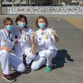 Des infirmières des Hôpitaux Universitaires de Genève (HUG) posent devant une banderole "Tenez Bon, Merci Pour Tout!": elles remercient la population de les soutenir tous les soirs à 21h00. Genève, le 19 mars 2020. [Keystone - Martial Trezzini]
