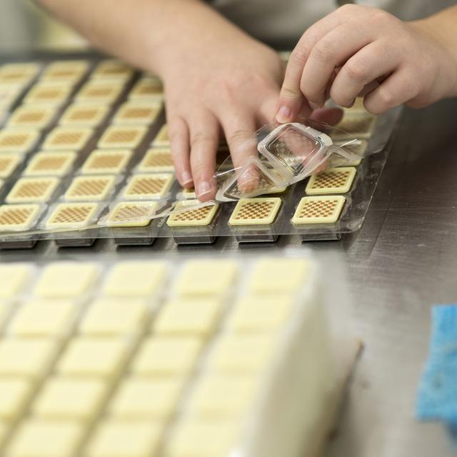 Une couverture de chocolat blanc est appliquée sur des pralinés dans le laboratoire de Läderach à Ennenda, dans le canton de Glaris (oct. 2013). [Keystone - Christian Beutler]