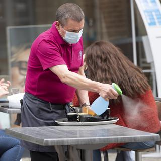 Un serveur désinfecte la table d'une cliente sur la terrasse d'un café-restaurant. [Keystne - Laurent Gillieron]