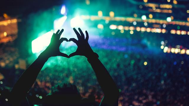 Une personne forme un coeur avec ses mains devant une scène de concert. [Depositphotos - bogdan.hoda]