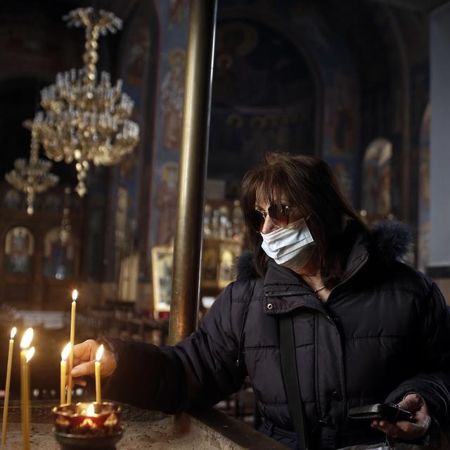 Une femme portant un masque de protection allume une bougie à l'intérieur d'une église orthodoxe à Athènes en Grèce. [Epa / Keystone - Kostas Tsironis]