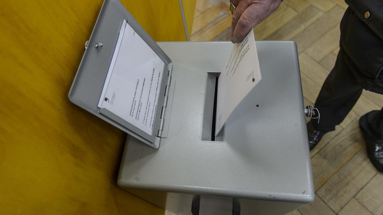 Une enveloppe de vote glissée dans l'urne dans le canton de Fribourg, en mars 2015. [Keystone - Jean-Christophe Bott]