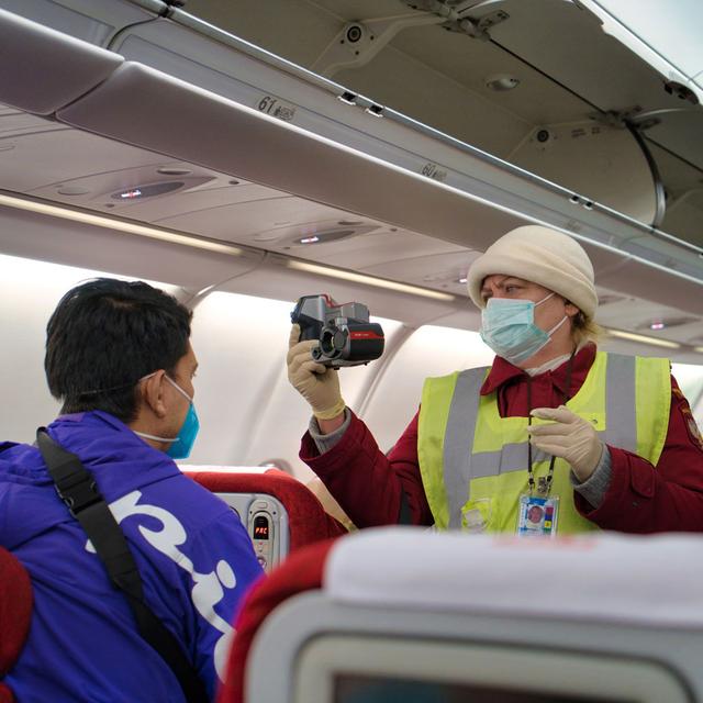 Une femme prend la température d'un passager grâce à une caméra thermique. [Depositphotos - IggySul]