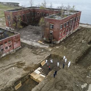 Des travailleurs vêtus d'un habit de protection enterrent des corps dans une tranchée sur Hart Island, dans le district du Bronx, à New York, le 9 avril 2020. [Keystone/AP photo - John Minchillo]