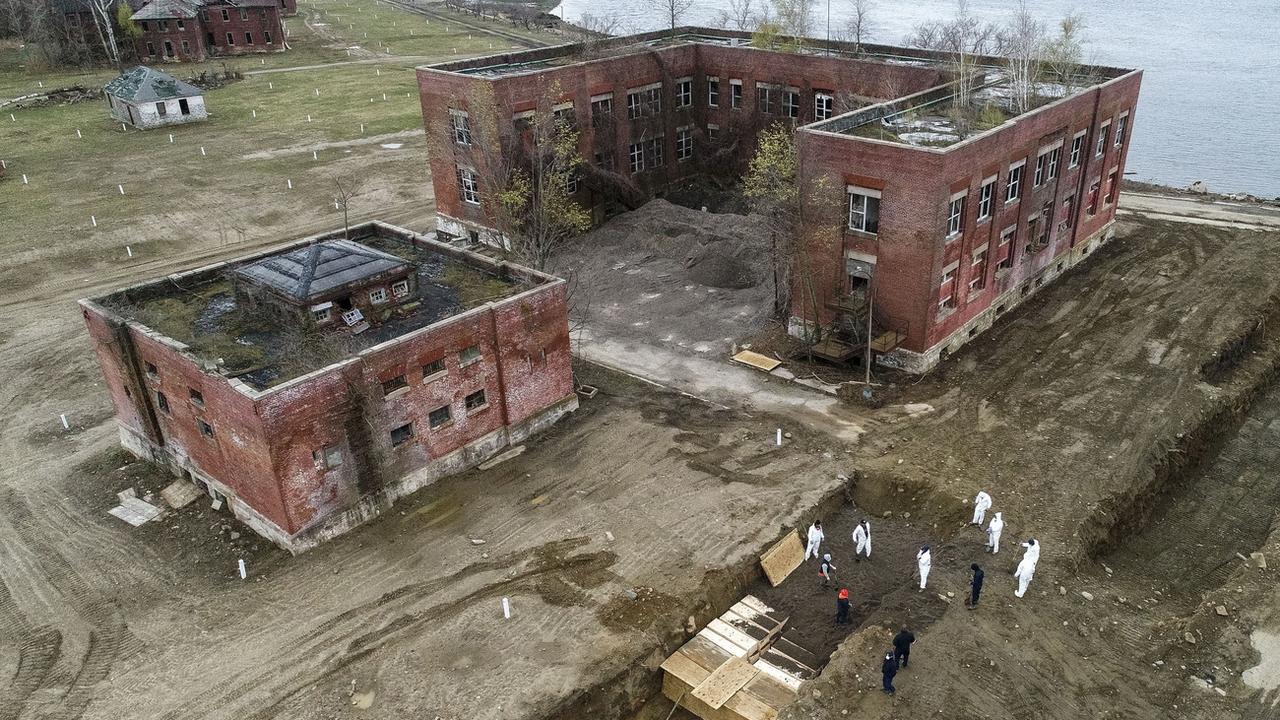 Des travailleurs vêtus d'un habit de protection enterrent des corps dans une tranchée sur Hart Island, dans le district du Bronx, à New York, le 9 avril 2020. [Keystone/AP photo - John Minchillo]