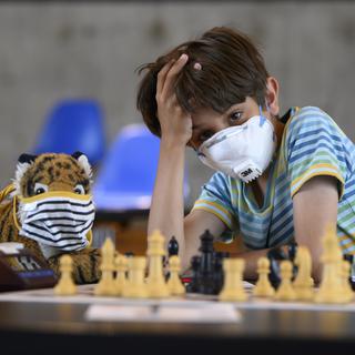 Un enfant masqué joue aux échecs. [Keystone - Anthony Anex]