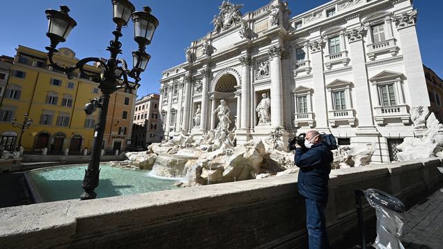 Un journaliste filmant la Fontaine de Trévi désertée suite aux mesures mises en place par l'Italie pour réduire la propagation du coronavirus. [AFP - Vincenzo Pinto]