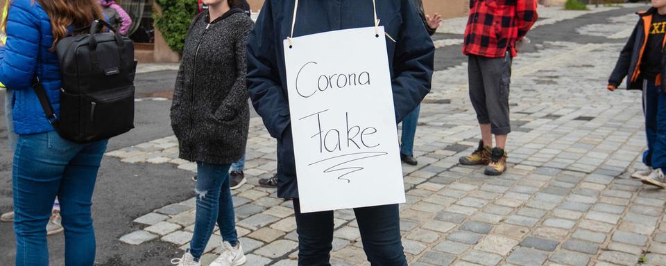 Un manifestant en Allemagne avec un panneau "Corona Fake". [Keystone - Nicolas Armer]