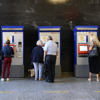 Des personnes achètent des billets à des distributeurs de billets à la gare CFF de Bienne. [KEYSTONE/Anthony Anex]