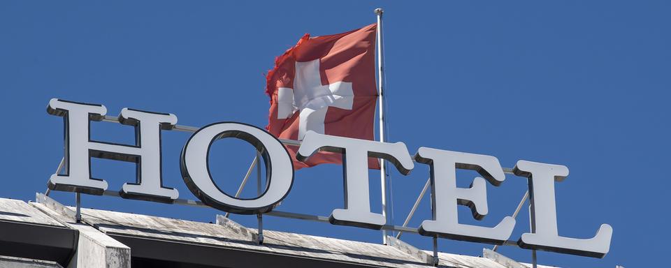 Le mot hôtel est photographie à coté du drapeau suisse, ce mercredi 5 août 2020 à Genève. [KEYSTONE - Martial Trezzini]