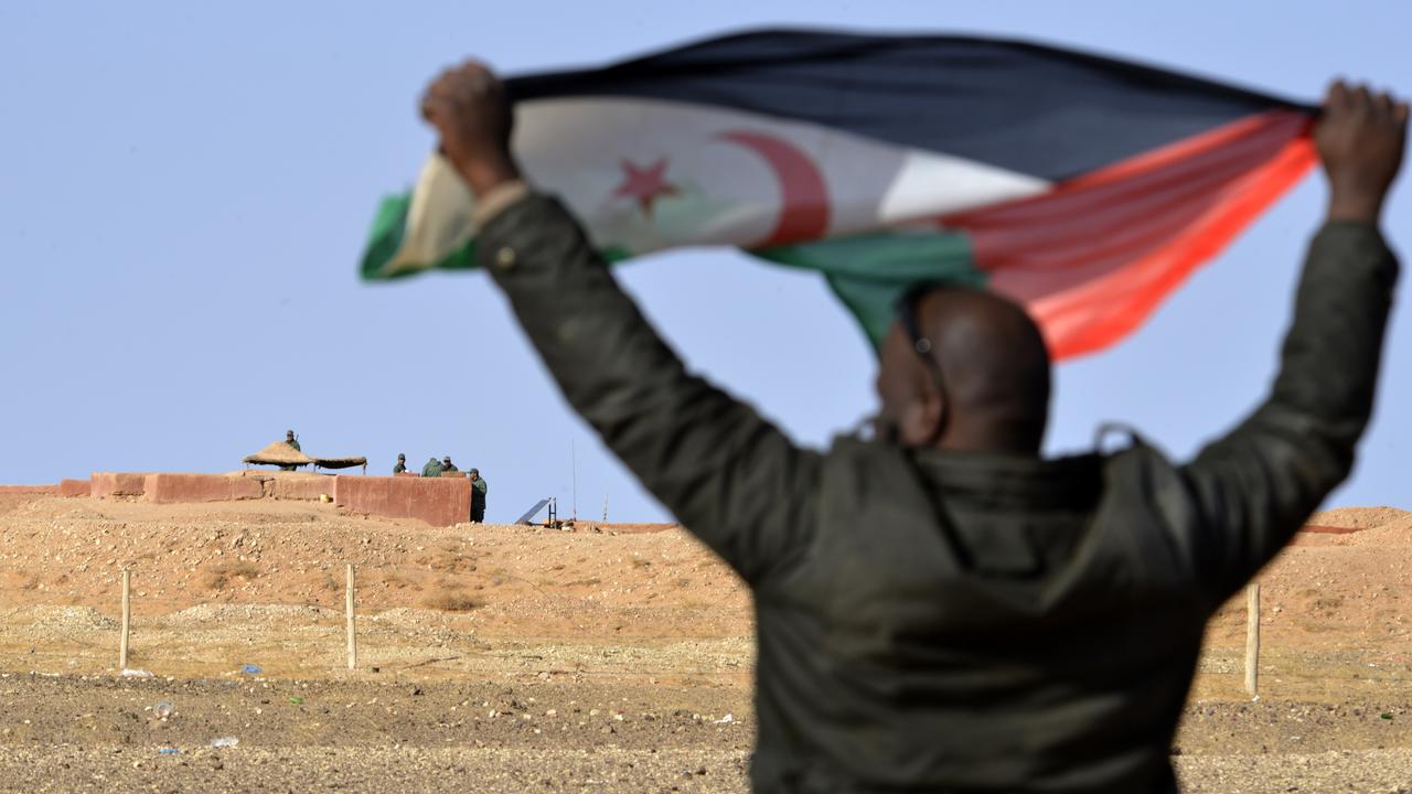 Un Sahraoui brandit le drapeau du Polisario, mouvement indépendantiste soutenu par l'Algérie, au-devant de soldats marocains qui garde un poste-frontière dans le Sahara occidental. [Stringer/AFP]