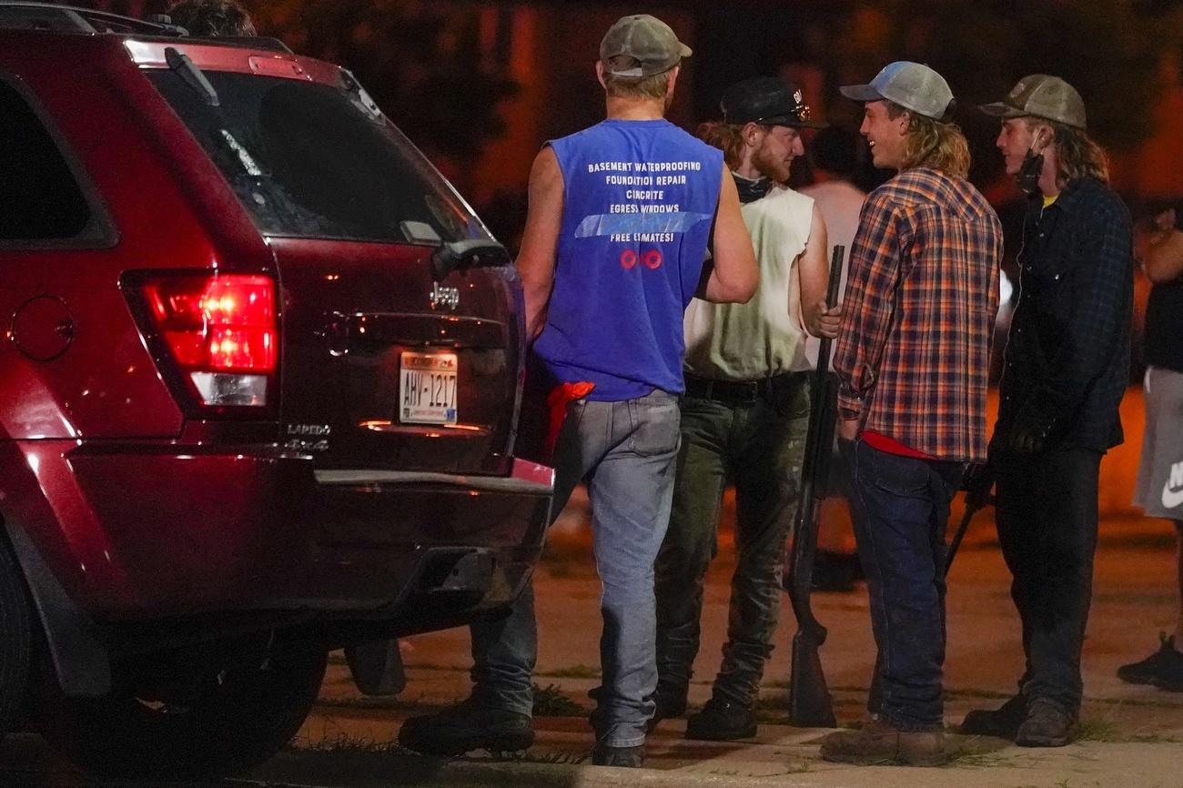 Un groupe d'hommes armés de fusils regardent les manifestants protestant contre la fusillade dont a été victime Jacob Blake. Kenosha, 25 août 2020. [Keystone/AP Photo - Morry Gash]