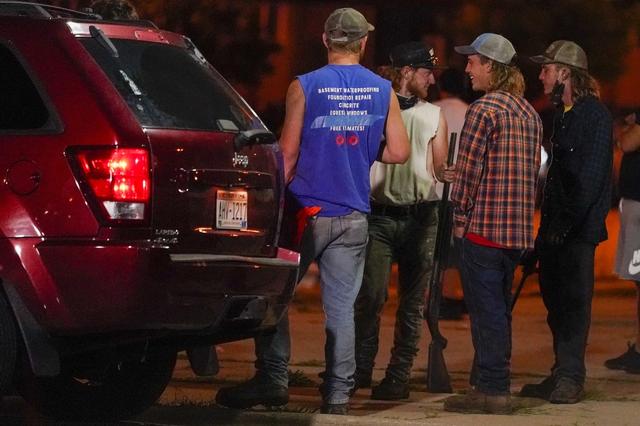 Un groupe d'hommes armés de fusils regardent les manifestants protestant contre la fusillade dont a été victime Jacob Blake. Kenosha, 25 août 2020. [Keystone/AP Photo - Morry Gash]