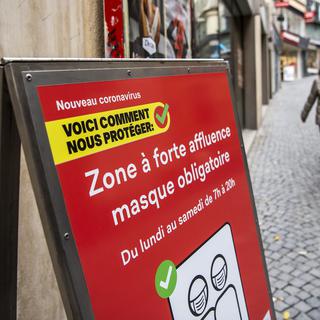 Une personne masquée près d'un panneau signalant une "zone à forte affluence", au centre-ville de Lausanne, le 10 novembre 2020. [Keystone - Jean-Christophe Bott]