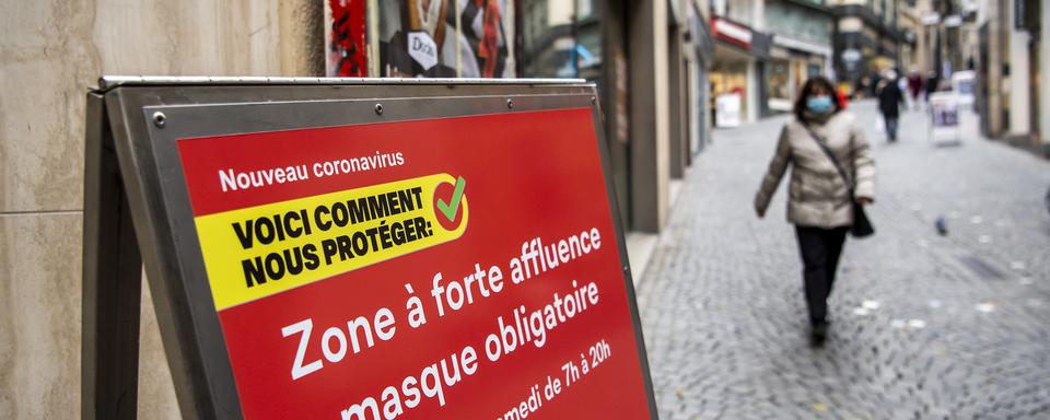 Une personne masquée près d'un panneau signalant une "zone à forte affluence", au centre-ville de Lausanne, le 10 novembre 2020. [Keystone - Jean-Christophe Bott]