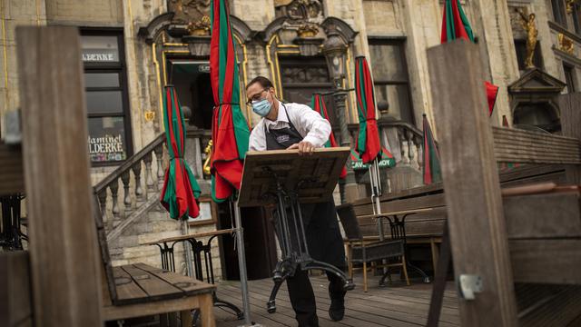 Un sommelier range le mobilier d'un café, au lendemain de nouvelles restrictions annoncées pour la ville de Bruxelles. [Keystone - Francisco Seco]