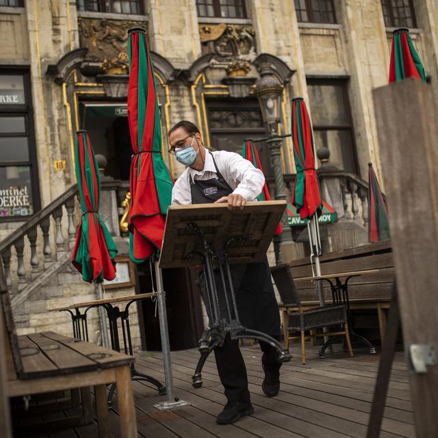 Un sommelier range le mobilier d'un café, au lendemain de nouvelles restrictions annoncées pour la ville de Bruxelles. [Keystone - Francisco Seco]