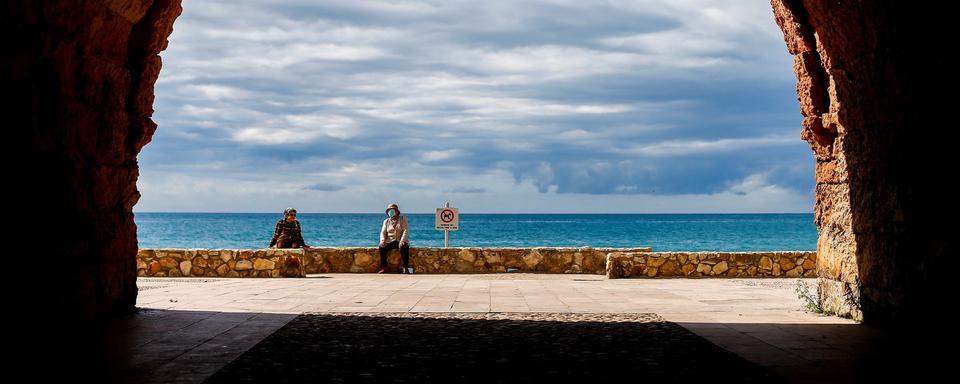 Deux personnes sont assises à distance près de la plage d'Altafulla, à Taragone en Espagne, le 13 mai 2020. [EPA/Keystone - Quique Garcia]