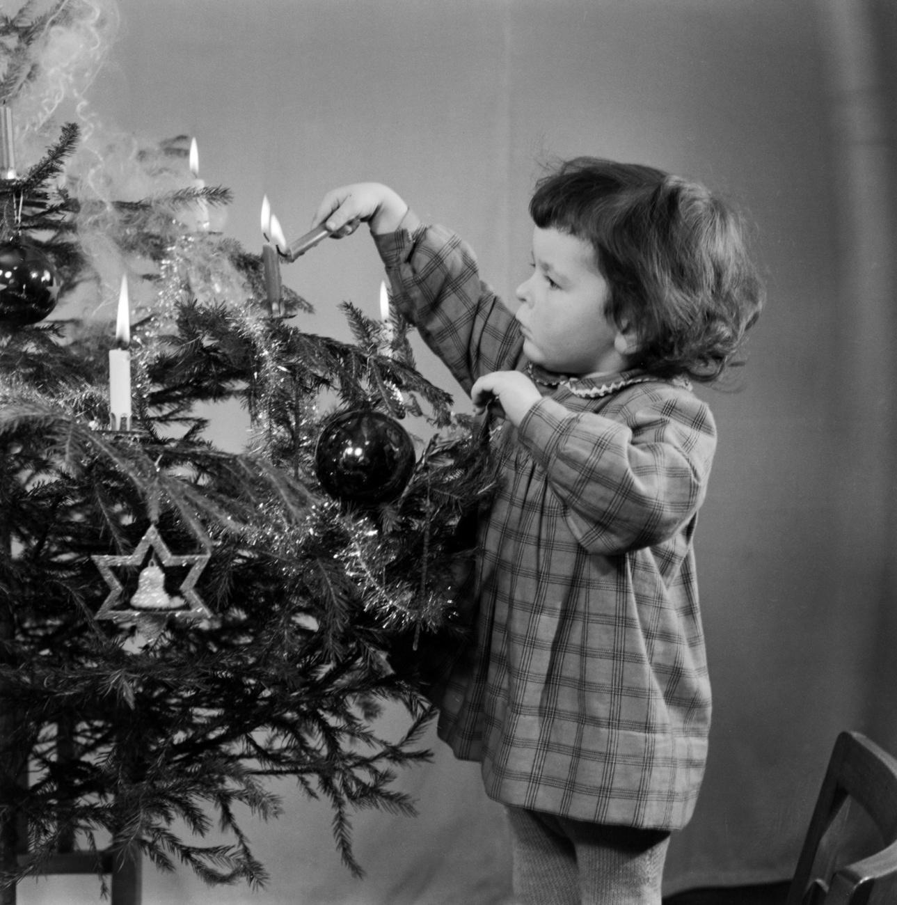 Petite fille allumant une bougie sur un sapin de Noël en 1953. [KEYSTONE - PHOTOPRESS-ARCHIV/KREBS]
