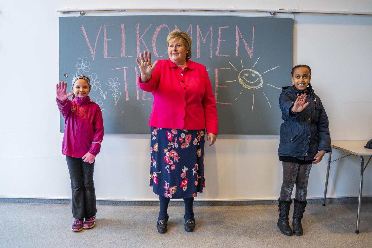 La Première ministre norvégienne, Erna Solberg, apprend de nouvelles manières de saluer grâce à deux élèves. L'image a été prise à Oslo le 27 avril, jour de réouverture des écoles pour les classes allant de la 1ère à la 4e année. Celles-ci avaient été fermées le 12 mars 2020. [Keystone/epa - Hakon Mosvold Larsen]