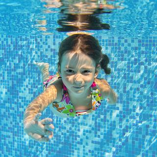 Une petite fille nage sous l'eau dans une psicine. [Depositphotos - JaySi]