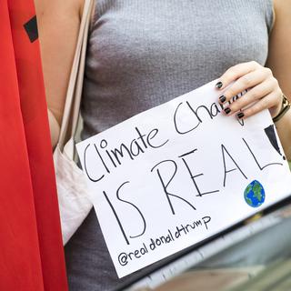 Une femme proteste avec une pancarte "Climate change is real @realdonaldtrump". [Keystone - Anthony Anex]