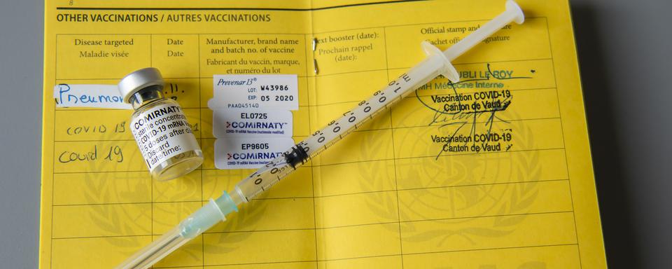 Une fiole du vaccin Pfizer-BioNTech et une seringue sont photographiées sur un carnet de l'OMS de certificat international de vaccination. [Keystone - Martial Trezzini]