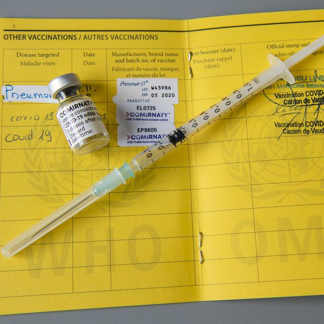 Une fiole du vaccin Pfizer-BioNTech et une seringue sont photographiées sur un carnet de l'OMS de certificat international de vaccination. [Keystone - Martial Trezzini]