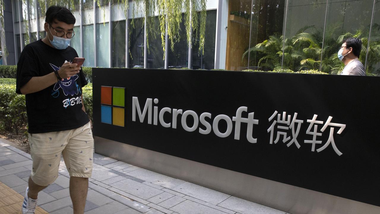 Un homme regarde son téléphone devant le siège de Microsoft à Pékin. [KEYSTONE - Ng Han Guan / AP Photo]