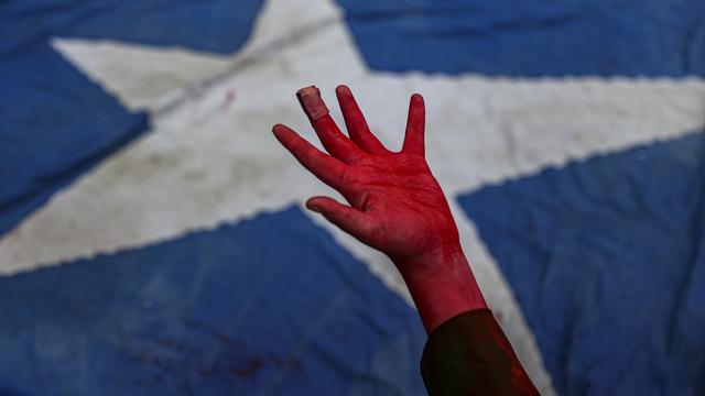 Une performance montre une main couverte de peinture rouge, symbolisant le sang, devant un drapeau chilien pour rendre hommage aux manifestants tués lors des manifestations de 2019 au Chili. [KEYSTONE - Esteban Felix / AP Photo]